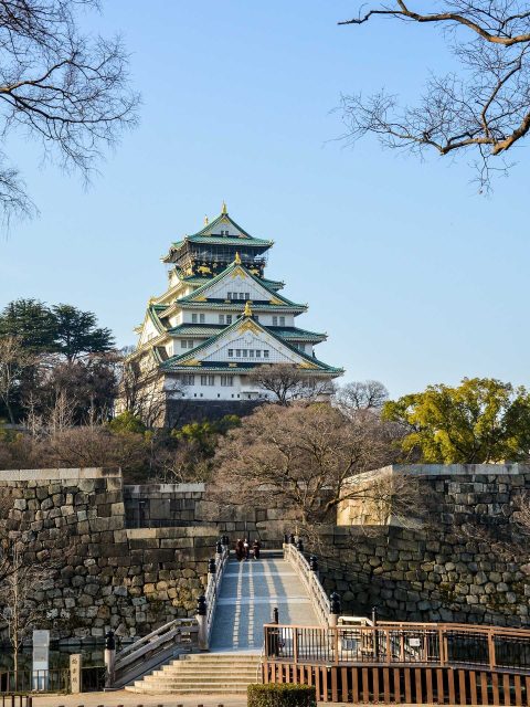 How to visit Osaka Castle: A stunning view of Osaka Castle, surrounded by moats and lush greenery, showcasing its historical grandeur.