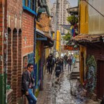 Things to Visit in Bogota: A vibrant street view of La Candelaria, the famous historic neighborhood in Bogotá, Colombia, featuring colorful buildings and street art.
