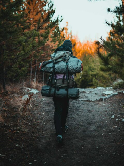 Beginner backpacker on a trail with a fully packed backpack, ready for a backpacking trip for beginners, surrounded by beautiful forest scenery.