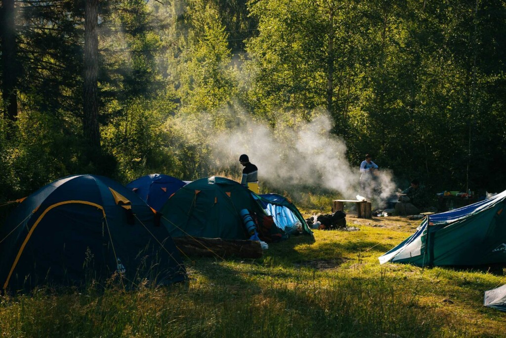 A group of campers enjoying a campsite in a lush green forest, with tents set up and a campfire smoking in the background—perfect for a camping guide for beginners.