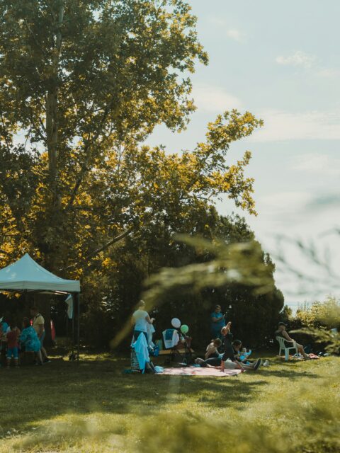 A group of people enjoying a sunny day at a campsite, with a tent, canopy, and picnic setup—perfect for those searching for tent camping near me and family-friendly camping spots.